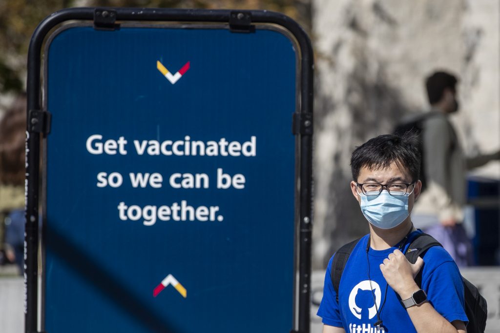 A person wears a mask to protect them from the COVID-19 virus while walking past COVID-19 vaccine information