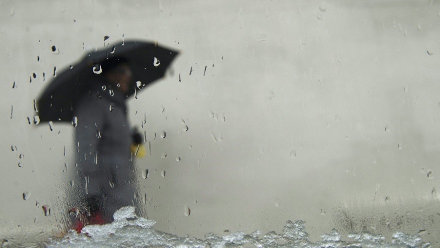 A person takes cover with their umbrella as both snow and rain fall