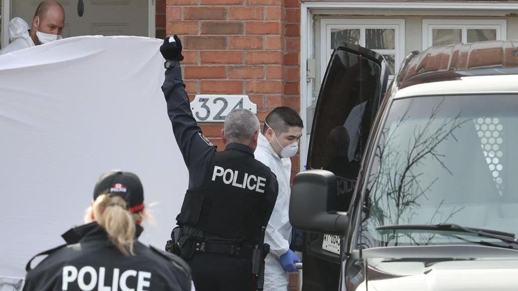 Police officers hold up a sheet as members of the coroner's office remove a body at the scene of a homicide where six people were found dead in the Barrhaven suburb of Ottawa on March 7, 2024