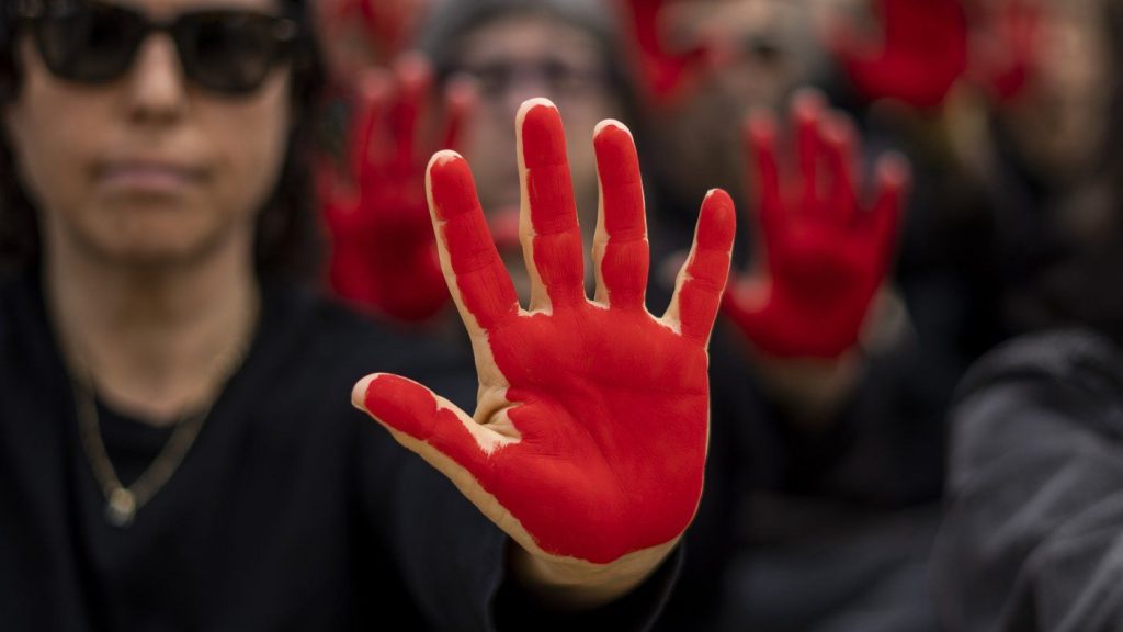 Family and supporters of hostages held in the Gaza Strip hold up their hands, painted red