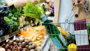 woman in white coat holding green shopping cart