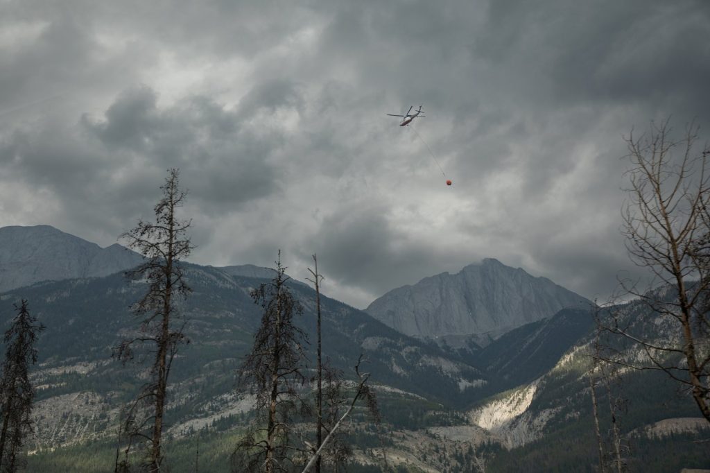 A helicopter buckets water onto smouldering fires outside of Jasper